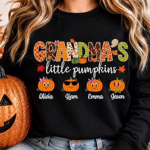 May include: A black long-sleeve sweatshirt featuring the text GRANDMA'S little pumpkins in colorful autumn-themed patterns. Below the text are four orange pumpkin illustrations with faces, labeled with the names Olivia, Liam, Emma, and Jason.