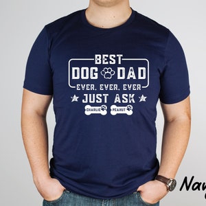 May include: Navy blue t-shirt with white text that reads "BEST DOG DAD EVER. EVER. EVER. JUST ASK" with a paw print graphic. Below the text are two dog bone graphics with the names "CHARLIE" and "PEANUT".