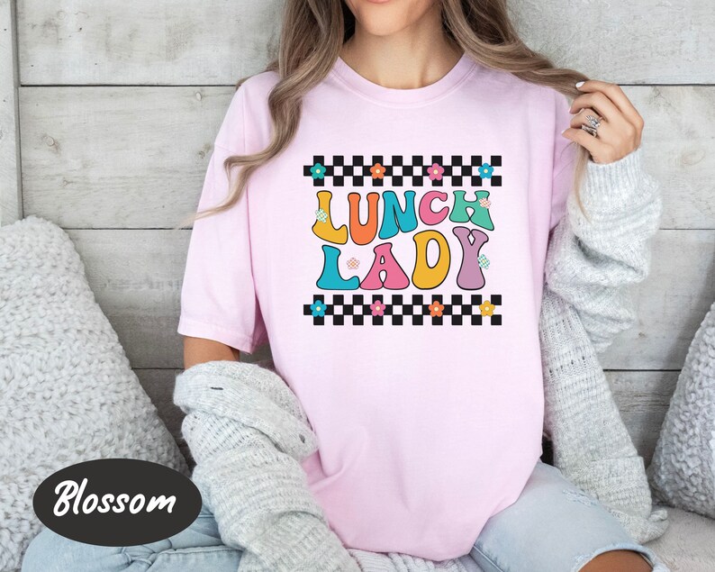 May include: Pink t-shirt with a checkered background and the text "Lunch Lady" in colorful, retro-style letters.
