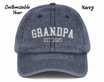 May include: Navy blue baseball cap with the word "GRANDPA" embroidered in white, along with "EST. 2025". The hat has a curved brim and a vintage, worn look. The text "Customizable Year" is above the hat.