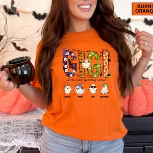May include: A burnt orange t-shirt featuring a graphic with the text "This GIGI Loves her spooky crew". The design includes large letters filled with Halloween patterns, a witch hat, and four ghost characters with the names Sophia, Emma, Max, and Benjamin.
