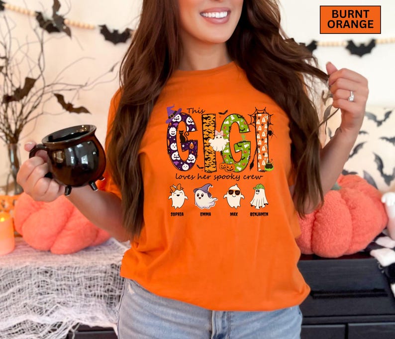 May include: A burnt orange t-shirt featuring a graphic with the text "This GIGI Loves her spooky crew". The design includes large letters filled with Halloween patterns, a witch hat, and four ghost characters with the names Sophia, Emma, Max, and Benjamin.