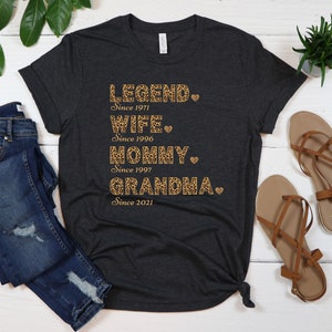 May include: A dark grey t-shirt with a leopard print design and the text "LEGEND. Since 1971 WIFE. Since 1996 MOMMY. Since 1997 GRANDMA. Since 2021"