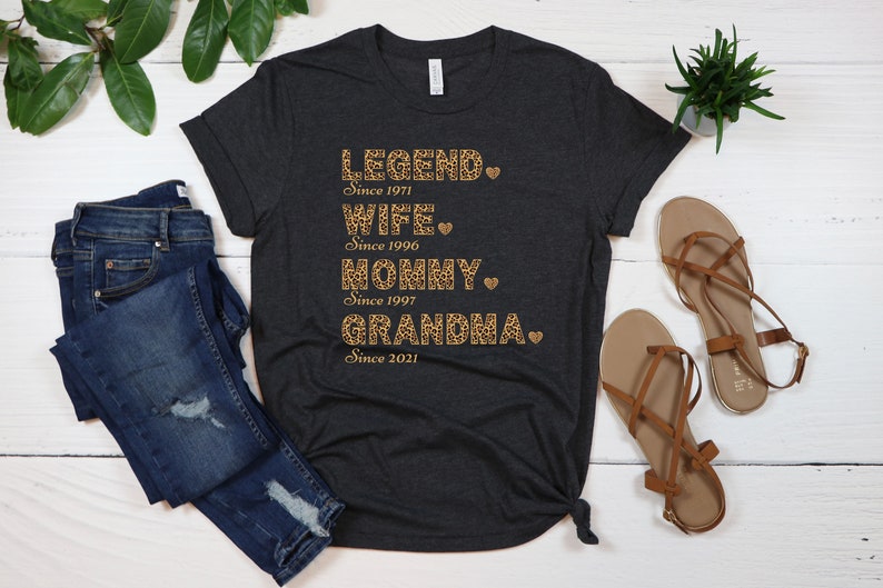 May include: A dark grey t-shirt with a leopard print design and the text "LEGEND. Since 1971 WIFE. Since 1996 MOMMY. Since 1997 GRANDMA. Since 2021"