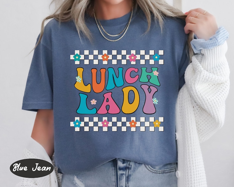 May include: A blue t-shirt with a checkered border and the text "Lunch Lady" in colorful, retro-style letters.