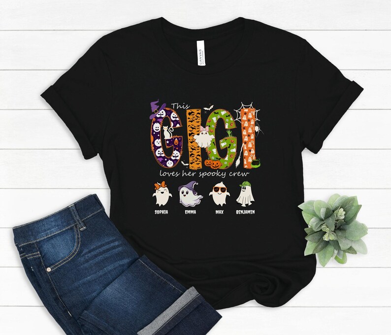 May include: A black short-sleeved t-shirt featuring the text "This GIGI loves her spooky crew" in large, patterned letters. Below the text are four cartoon ghosts with names "Sophia", "Emma", "Max", and "Benjamin" printed underneath each.