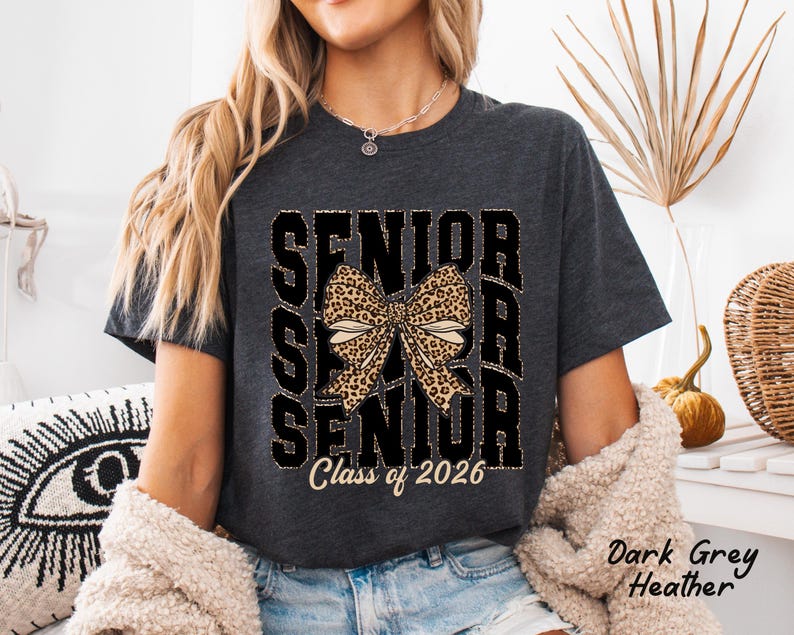 Puede incluir: Camiseta de color gris oscuro jaspeado con un gr&aacute;fico negro de la palabra "Senior" repetida tres veces con un lazo de estampado de leopardo en el centro y el texto "Class of 2026" debajo.