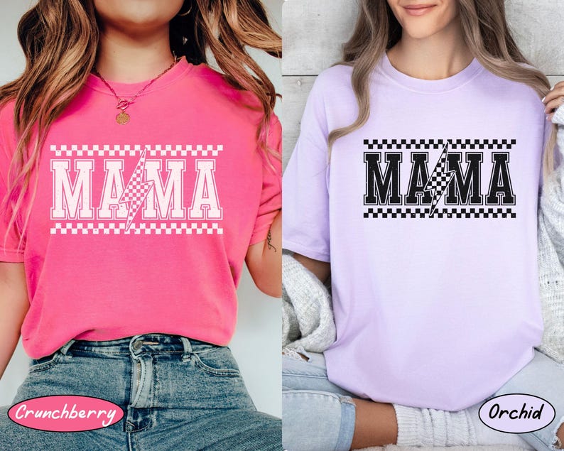 May include: Two short-sleeved t-shirts, one pink and one lavender, each with the word "MAMA" in bold, white, block letters. A lightning bolt graphic is in the center. The word is framed by a checkered pattern.