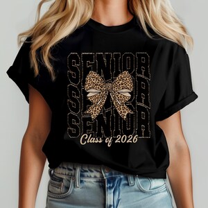 Puede incluir: Camiseta negra con un gr&aacute;fico de la palabra "Senior" repetida tres veces con un lazo de estampado de leopardo en el centro. El texto "Class of 2026" est&aacute; impreso debajo del gr&aacute;fico.