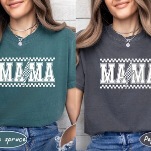 May include: Two t-shirts, one blue-green and one gray, each with the word "MAMA" in white block letters. A lightning bolt graphic with a checkered pattern is in the center of the word. The top and bottom of the word are bordered with a checkered pattern.