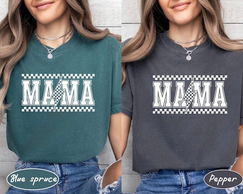 May include: Two t-shirts, one blue-green and one gray, each with the word "MAMA" in white block letters. A lightning bolt graphic with a checkered pattern is in the center of the word. The top and bottom of the word are bordered with a checkered pattern.