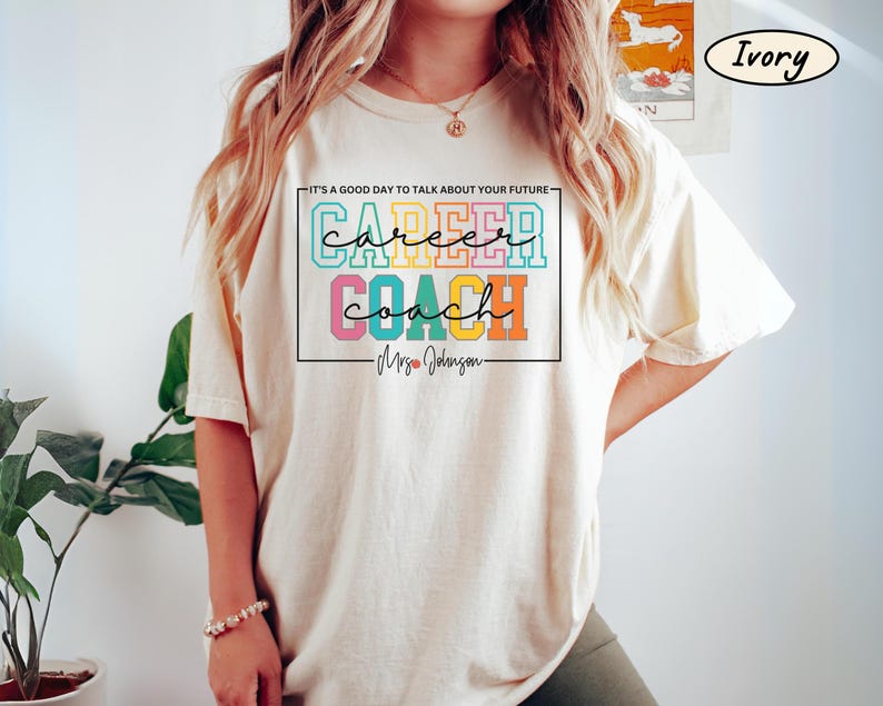 May include: Ivory t-shirt with a colourful graphic that says "IT'S A GOOD DAY TO TALK ABOUT YOUR FUTURE - career coach - Mrs. Johnson - "