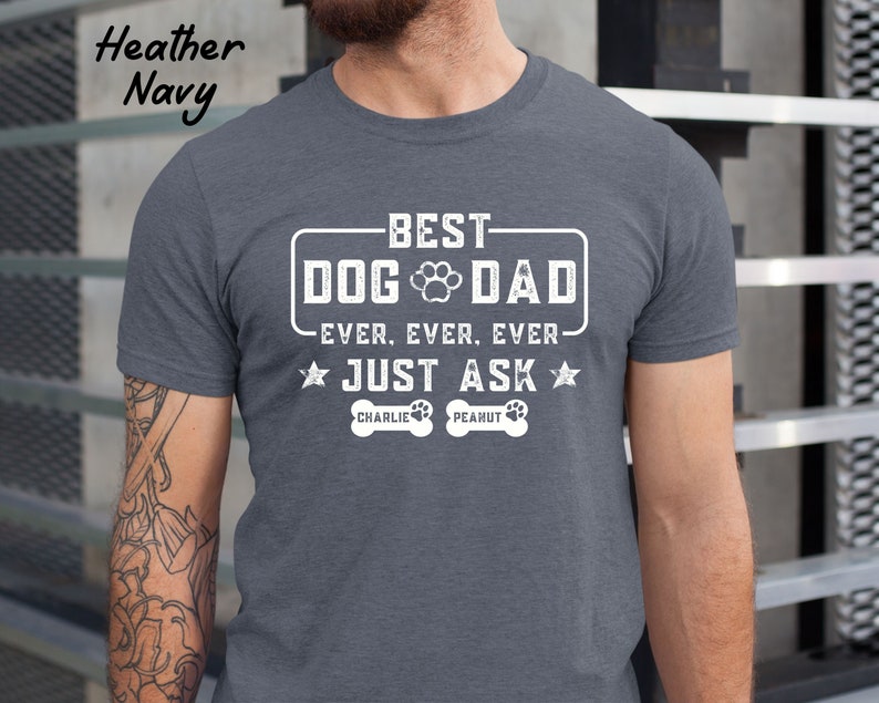 May include: Heather navy t-shirt with the text "BEST DOG DAD EVER. EVER. EVER. JUST ASK". The design includes a paw print and two dog bone graphics with the names "Charlie" and "Peanut".