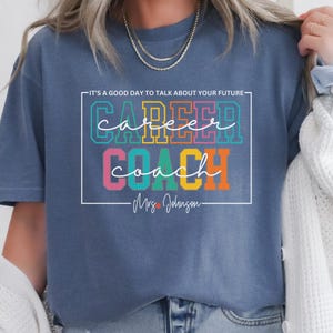 May include: A blue t-shirt with the text "It's a good day to talk about your future" above the text "Career Coach" in rainbow colours. The text "Mrs. Johnson" is below the rainbow text.
