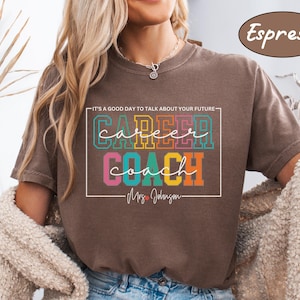 May include: A brown t-shirt with the text "It's a good day to talk about your future - Career Coach - Mrs. Johnson" in a colourful, rectangular box. The text is in a rainbow colour scheme.