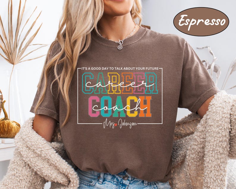 May include: A brown t-shirt with the text "It's a good day to talk about your future - Career Coach - Mrs. Johnson" in a colourful, rectangular box. The text is in a rainbow colour scheme.