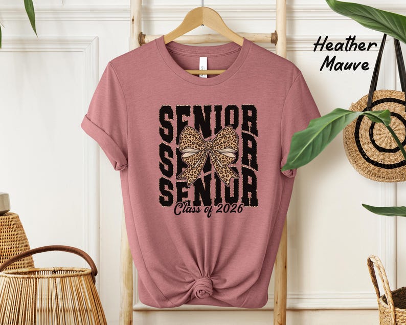 Puede incluir: Una camiseta de color malva jaspeado con un gr&aacute;fico negro que dice "Senior" tres veces con un lazo de estampado de leopardo en el medio. El texto "Class of 2026" est&aacute; debajo del gr&aacute;fico.