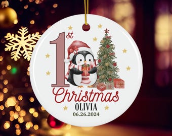 Puede incluir: Adorno navideño redondo blanco con un pingüino sosteniendo un regalo, un árbol de Navidad y el texto "1er Navidad Olivia 06.26.2024".