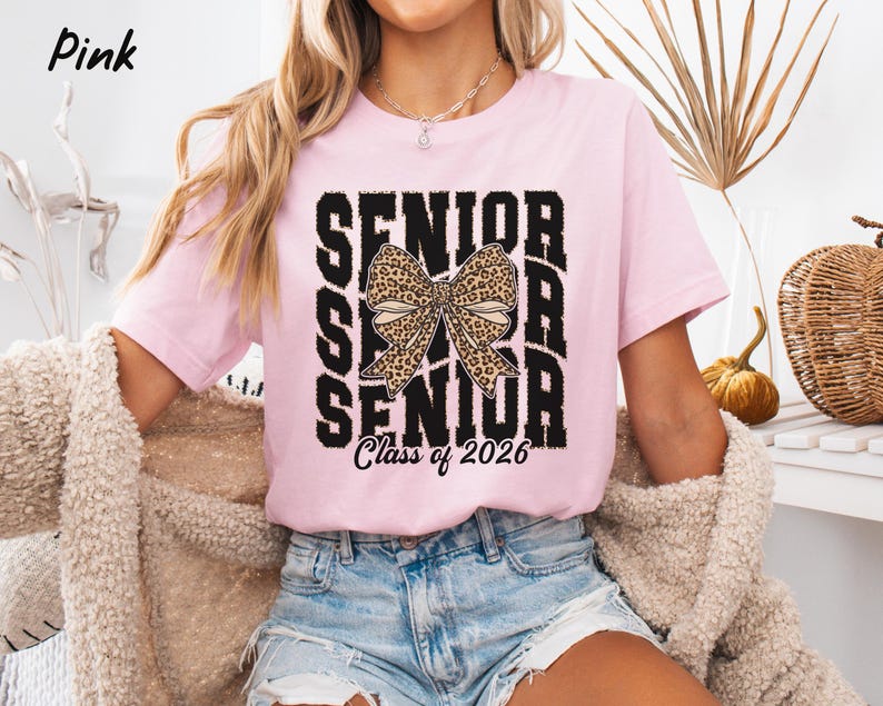 Puede incluir: Camiseta rosa con un gr&aacute;fico en blanco y negro que dice "Senior" con un lazo de estampado de leopardo en el medio y "Class of 2026" en la parte inferior.