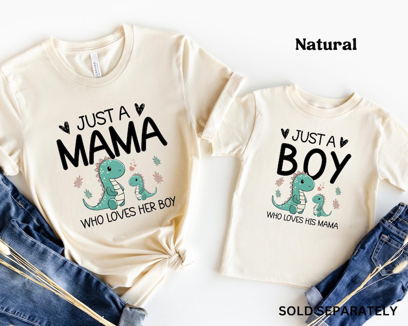 May include: Two cream coloured t-shirts with a dinosaur graphic and text that reads "Just a Mama who loves her boy" and "Just a Boy who loves his mama".