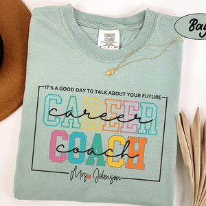 May include: A light blue t-shirt with the text "It's a good day to talk about your future" above the words "career coach" in colourful block letters. The text "Mrs. Johnson" is below the words "career coach".