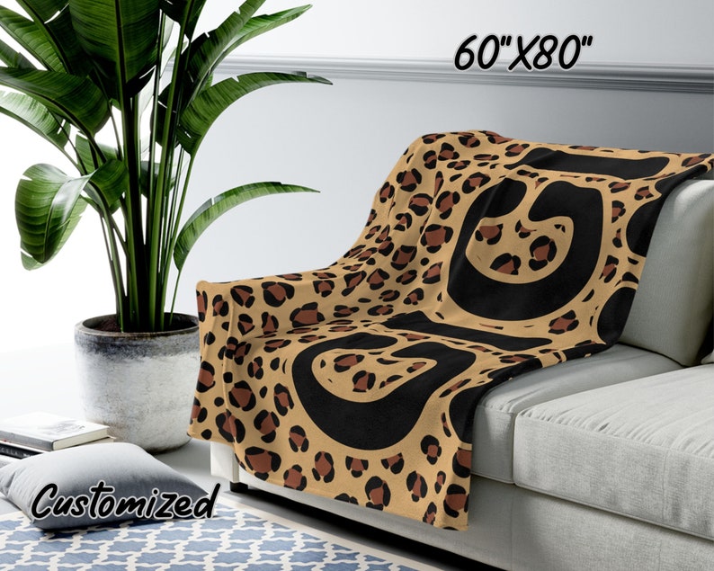 K&ouml;nnte beinhalten: Eine braune und schwarze Leopardenfell-Decke mit schwarzen abstrakten Formen. Die Decke ist 152,4 cm x 203,2 cm gro&szlig; und liegt auf einem Sofa.