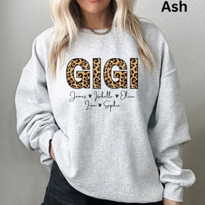 May include: Grey sweatshirt with the word "GIGI" in large, leopard print letters. Below the word are the names "James, Isabella, Olivia, Liam, Sophie" with hearts between each name.