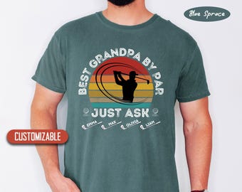May include: A teal green t-shirt with a vintage-style graphic of a golfer teeing off. The text reads "Best Grandpa By Par Just Ask" with the names Emma, Max, Olivia, and Liam below.