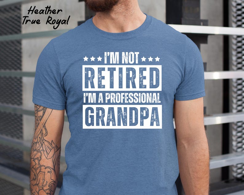 May include: Heather True Royal blue t-shirt with the text "I'M NOT RETIRED I'M A PROFESSIONAL GRANDPA" in white block letters. The shirt has a crew neck and short sleeves. The shirt is made of a soft, comfortable material.