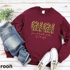 May include: Maroon sweatshirt with the word "GIGI" in leopard print letters. Below the word are the names "James, Johella, Olivia, Liam, Sophia" with hearts between each name.