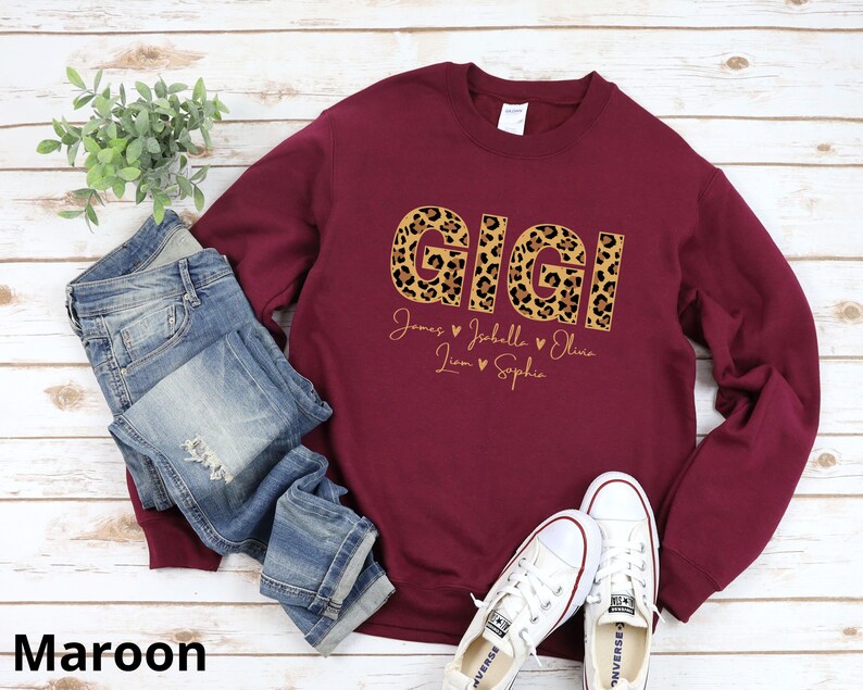May include: Maroon sweatshirt with the word "GIGI" in leopard print letters. Below the word are the names "James, Johella, Olivia, Liam, Sophia" with hearts between each name.