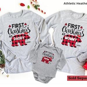 May include: Two athletic heather gray long-sleeve shirts and one matching long-sleeve bodysuit. Each garment features a red and black buffalo plaid bear graphic with a Santa hat, the text "FIRST CHRISTMAS AS" or "MY FIRST CHRISTMAS", and "2026".
