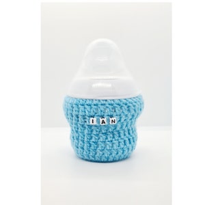 May include: A blue crocheted bottle cover with the name "IAN" spelled out in white letters.