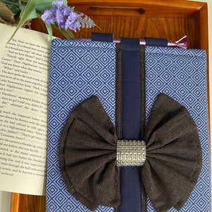May include: A blue and white patterned fabric journal with a brown bow and a silver rhinestone accent. The journal has a navy blue border and the text "OMT" printed on the front.