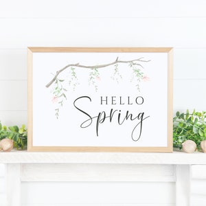 May include: A framed print featuring a watercolour illustration of a branch with delicate pink flowers and green leaves. The text "Hello Spring" is written in black cursive lettering.