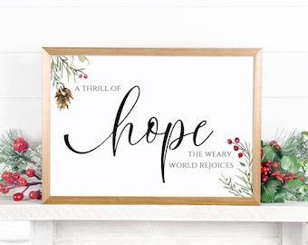 May include: A framed print with a gold frame and a white background. The print features a watercolor illustration of pine branches and berries. The text reads "A thrill of hope, the weary world rejoices."