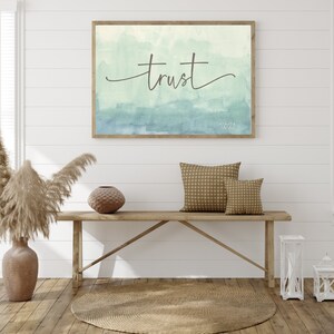 May include: A framed watercolor painting with a light blue and green gradient background. The word "trust" is written in cursive in the center of the painting. The year "2021" is written in the bottom right corner of the painting.