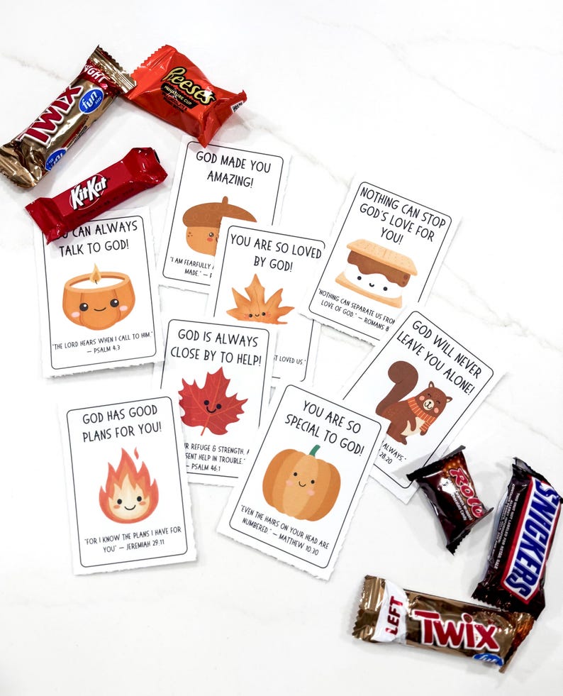 Op de afbeelding: Een assortiment chocoladerepen en kaarten met inspirerende boodschappen en schattige illustraties. De kaarten tonen afbeeldingen van een kaars, eikel, blad, s'more, esdoornblad, eekhoorn, vuur en pompoen. De chocoladerepen zijn onder andere Kit Kat, Reese's, Twix en Snickers.