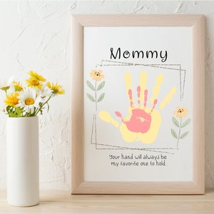 May include: A framed print with a handprint in yellow and pink paint. The print says "Mommy" and "Your hand will always be my favorite one to hold."