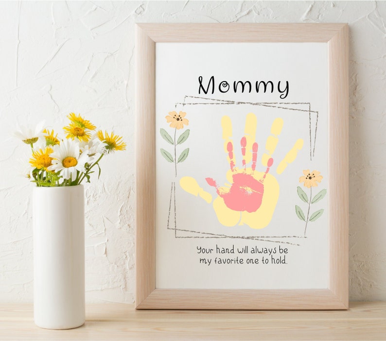 May include: A framed print with a handprint in yellow and pink paint. The print says "Mommy" and "Your hand will always be my favorite one to hold."