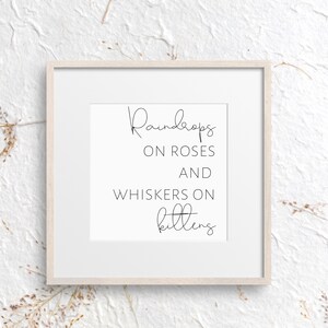 May include: A framed print with the words "Raindrops on Roses and Whiskers on Kittens" in elegant black script. The print is set in a white mat and a light wood frame, against a textured white background.