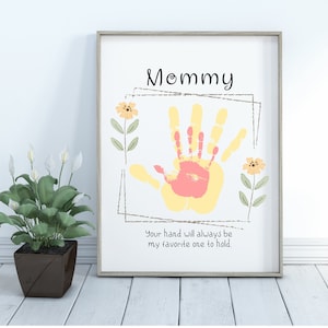 May include: A white framed print with a yellow and pink handprint in the center. The print says "Mommy" at the top and "Your hand will always be my favorite one to hold." at the bottom.