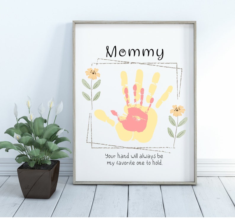 May include: A white framed print with a yellow and pink handprint in the center. The print says "Mommy" at the top and "Your hand will always be my favorite one to hold." at the bottom.