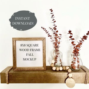 May include: A brown wooden 8x8 square frame with a white mat and the text "8x8 SQUARE WOOD FRAME FALL MOCKUP" on a wooden shelf with a wooden bead garland and two glass vases with dried eucalyptus branches.
