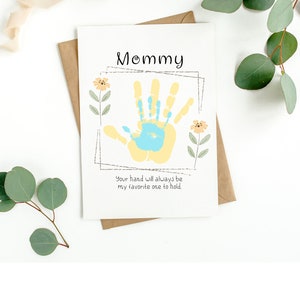 May include: A white card with the words "Mommy" in black script. A yellow handprint with a blue handprint inside is in the center of the card. The text "Your hand will always be my favorite one to hold." is below the handprint.