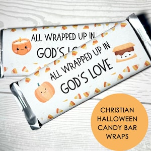 May include: Two rectangular candy bars wrapped in white paper featuring a repeating pattern of orange, yellow, and white candy corn. The wrappers display the text ALL WRAPPED UP IN GOD'S LOVE, accompanied by illustrations of a pumpkin and a s'more.