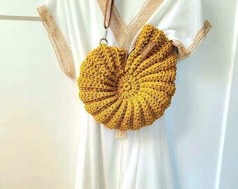 May include: A crocheted yellow seashell-shaped bag with a brown strap and a white tassel. The bag is hanging on a white dress with a lace trim.