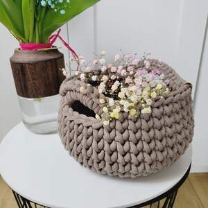 May include: A brown crocheted basket with a small opening at the top. The basket is filled with a bouquet of small pink and white flowers.