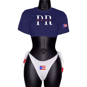 May include: A navy blue crop top with short sleeves and the text "PR PUERTO RICO" in white. The top has a red and white Puerto Rican flag on the right sleeve. A white bikini bottom with a red and white Puerto Rican flag on the front.