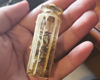 May include: A small glass bottle filled with dried herbs and gold glitter, sealed with a clear wax top.